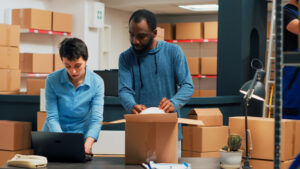 worker preparing shipping box with woman using laptop